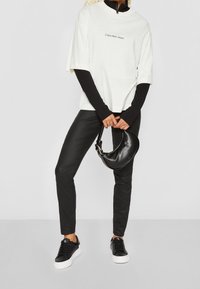 Biały oversize’owy t-shirt z logo "Calvin Klein Jeans", czarne dopasowane spodnie, czarne trampki i mała czarna torebka.