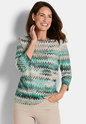 Langarmshirt mit einem wellenförmigen Zickzack-Muster in Blaugrün, Schwarz und Creme. Weicher Stoff mit Rundhalsausschnitt und Dreiviertelärmeln.