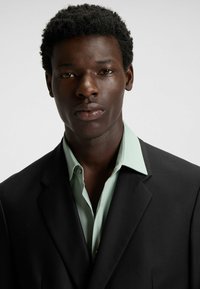 Black suit jacket over a light green collared shirt. Smooth fabric texture, sharp collar details, and a neutral background.
