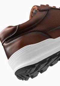 Bruine leren sneakers met een gestructureerde bovenkant, een witte tussenzool en een zwarte rubberen loopzool met een patroon in het profiel.