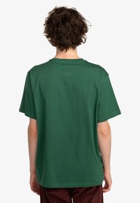 Camiseta de algodón de manga corta y cuello redondo en color verde oscuro con un corte holgado. Textura suave, sin detalles de diseño visibles. Vista trasera.