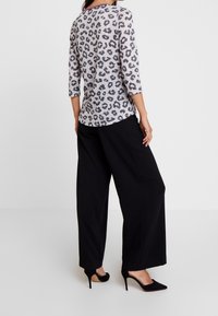 Haut gris clair à imprimé léopard avec manches trois-quarts, associé à un pantalon noir à jambes larges et des chaussures à talons noirs. Texture de tissu lisse.