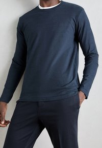Granatowa, długosleeve koszula z miękkiego bawełnianego materiału, z okrągłym dekoltem i subtelnym logo na piersi, w połączeniu z teksturowanymi ciemnymi spodniami.