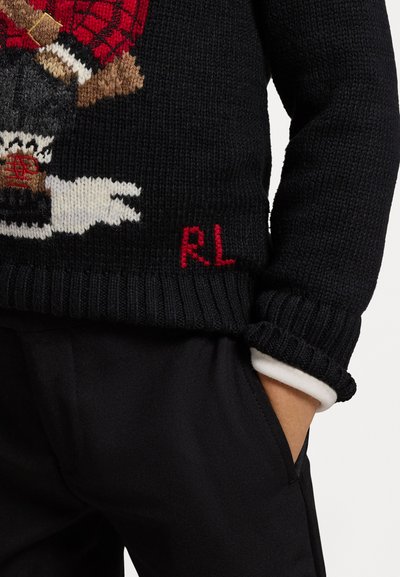 Sweater preto tricotado com um padrão texturizado, apresentando um design bordado e a letra "R.L." em vermelho na bainha, usado com calças pretas.
