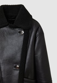 Giubbotto di pelle nera con colletto in finta pelliccia nera, texture liscia, due bottoni e design contemporary.