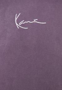 Fialová bavlněná látka s hladkou texturou, zdobená bílým vyšívaným nápisem "Kani" výrazně umístěným.