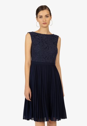 Mörkblå klänning med spetsliv och ärmlös design, med en veckad kjol och en väldefinierad midja som skapar en elegant silhuett.