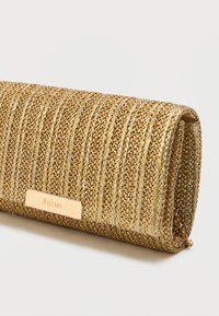 Kuldne kudumine klapp, millel on tekstuuriga pind, metallne klamber ja väike kett, kavandatud ristkülikukujuliseks.