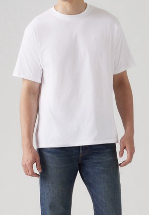 White cotton T-shirt with a round neck and short sleeves, featuring a subtle embossed logo on the chest. Worn with blue jeans.