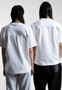 Witte katoenen t-shirts van achteraf getoond, met een recht model, korte mouwen en minimale stikdetails. Zwarte broeken met logodetail.