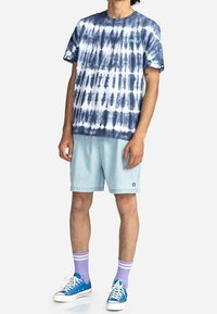 Blå och vit tie-dye kortärmad t-shirt, ihop med ljus denimshorts, blå sneakers och lila-randiga strumpor.