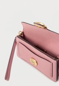 Rózsaszín bőrpénztárca sima felülettel, arany színű kör alakú kapoccsal, csuklópánttal és több kártyatartó rekesszel a belsejében.