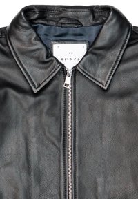Giacca in pelle nera con colletto a punta, chiusura centrale con zip e finitura testurizzata. L'interno è foderato con un tessuto liscio e presenta un'etichetta.