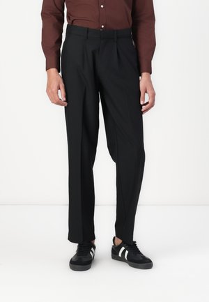 Pantalon noir ajusté à coupe droite, avec une texture lisse et des plis, associés à des baskets noires à rayures blanches.