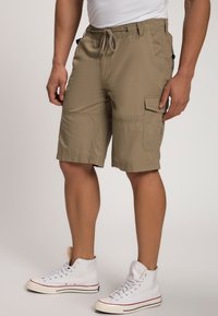 Pantalones cortos cargo beige con cintura elástica y cordón, con bolsillos laterales y un corte relajado. Combinados con zapatillas altas blancas.