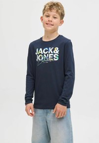 Tricou cu mânecă lungă de culoare bleumarin cu grafică "JACK & JONES" în litere colorate de tip bloc. Material din bumbac cu guler rotund, asortat cu blugi deschiși.