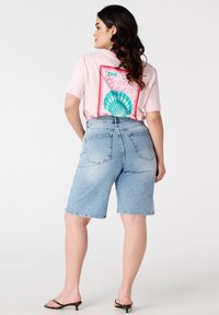 T-shirt rose clair à manches courtes avec un graphique coloré en forme de coquillage et du texte au dos, associé à un short en denim bleu taille haute.