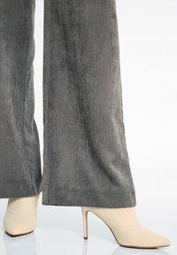 Beige hoge hakken met een textured stoffen bovendeel en een spitse neus, gecombineerd met grijze corduroy wijde broek met verticale strepen.