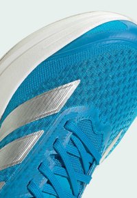 Niebieski but sportowy z teksturowaną siateczką, srebrnymi akcentami i wyściełaną podeszwą. Sznurowadła są wyraźnie widoczne.