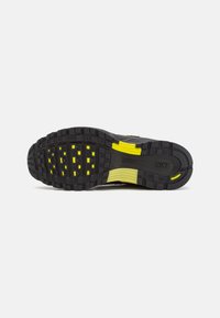 Black athletic shoe sole with textured rubber, featuring yellow detailing and a wave-like design for traction and flexibility.