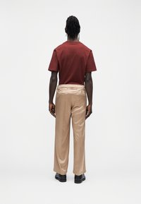 Bordowa koszulka z krótkim rękawem i okrągłym dekoltem, zestawiona z beżowymi, luźnymi spodniami i czarnymi butami. Strój widziany od tyłu.