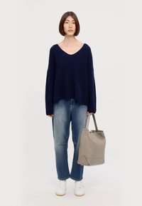 Maglione blu navy a coste con scollatura a V, vestibilità rilassata; jeans azzurri; sneakers bianche; borsa tote grigia. Design semplice e moderno con una texture morbida.