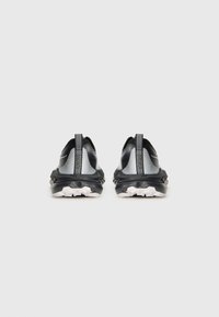 Chaussures de sport noires et argentées avec une tige en mesh, des accents réfléchissants, un col rembourré et une semelle en caoutchouc texturée. Tirant à l'arrière pour un enfilage facile.