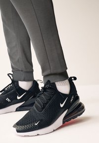 Fekete Nike Air Max sportcipők, hálós felsőrésszel, fehér logóval és látható légpárnás talppal; szürke sportnadrággal és fehér zoknival párosítva.