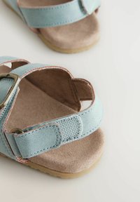 Sandali regolabili di colore azzurro chiaro con design a due cinturini, sottopiede tipo suede, suola in gomma e cuciture decorative lungo i bordi.