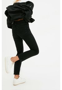 Jeans de mezclilla negra con un diseño ajustado, cinco bolsillos y una cintura alta, combinados con zapatillas blancas para crear contraste.