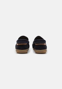 Navy Suede Slipper mit einer hellbraunen Gummisohle und genähten Details. Die Rückansicht zeigt einen weichen Kragen und ein Logo-Detail.