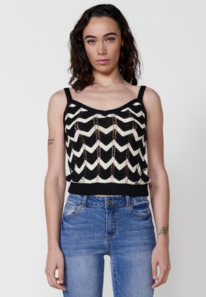 Černý a krémový pletený crop top se zigzag vzorem a tenkými ramínky, s vroubkovaným lemem. V kombinaci s modrými džíny.