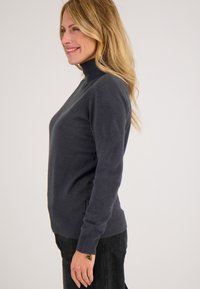 Donkergrijze trui met een hoge kraag, lange mouwen en een aansluitend design, gemaakt van zacht materiaal. Gladde textuur met minimale details.