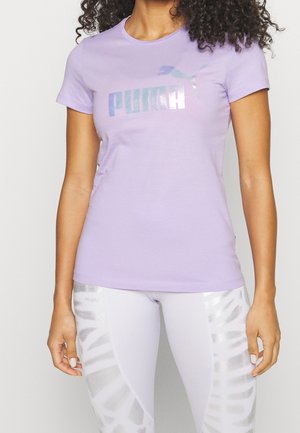 Kobieta w lawendowej koszulce Puma z metalicznym logo oraz białych legginsach z srebrnymi wzorami przypominającymi zebry.