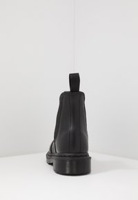 Black leather ankle boot with elastic side panels, textured rubber sole, and a pull tab at the back. Smooth finish and reinforced stitching.