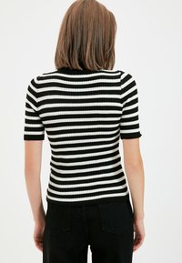Haut en tricot côtelé noir et blanc à rayures, à manches courtes et coupe ajustée, avec un col rond et un tissu texturé.