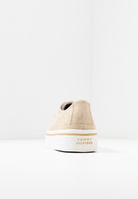 Sneaker in tela beige con tomaia testurizzata, suola in gomma bianca e accento del logo dorato sul tallone. Design minimalista con una forma classica.