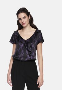 Black blouse with purple snake print, featuring a V-neck and ruffled neckline. Smooth fabric texture, relaxed fit, paired with black trousers.