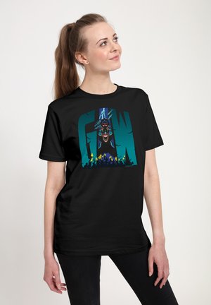 Giovane donna con coda di cavallo castana che indossa una maglietta nera con una grafica colorata di un volto minaccioso e una folla sotto le lettere "GN".