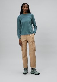 Camicia a maniche lunghe blu chiaro, pantaloni cargo beige con tasche laterali e scarpe da trekking verdi. Tessuto liscio e vestibilità comoda.