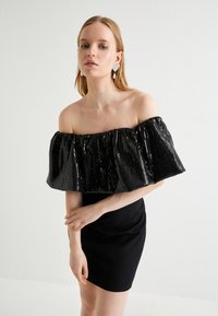 Robe noire décolletée avec un col en sequins et une finition froncée. La robe présente une coupe ajustée avec une longueur au genou.