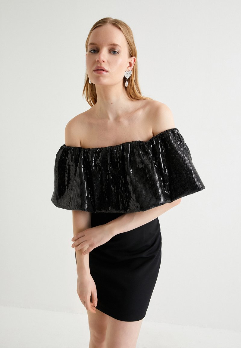Robe noire décolletée avec un col en sequins et une finition froncée. La robe présente une coupe ajustée avec une longueur au genou.