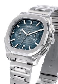 Montre en acier inoxydable avec un boîtier octogonal, un cadran texturé bleu foncé, trois sous-cadrans, des aiguilles argentées et un affichage de la date à 18 heures.