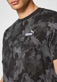 Zwarte t-shirt met korte mouwen met een grijs camouflagepatroon, voorzien van een wit Puma-logo op de linker borst en een gestructureerde afwerking.