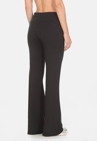 Pantaloni da yoga neri con un design a gamba svasata, realizzati in un materiale elastico. Presentano una vita alta e una texture liscia.