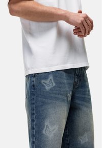 T-shirt bianco in cotone con orlo dritto abbinato a jeans in denim blu sbiadito con motivi di farfalle. Entrambi i capi hanno una vestibilità comoda.