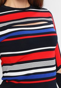 Gestreiftes Oberteil mit roten, weißen und blauen horizontalen Streifen. Verfügt über eine Aussparung in der Nähe des Halsausschnitts. Hergestellt aus weichem, dehnbarem Stoff.