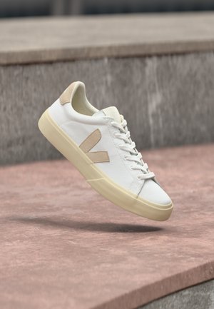 Biały trampki z beżowymi akcentami, z gładką cholewką, okrągłym noskiem i teksturowaną gumową podeszwą. Sznurowadła i logo w pasującym beżowym kolorze.