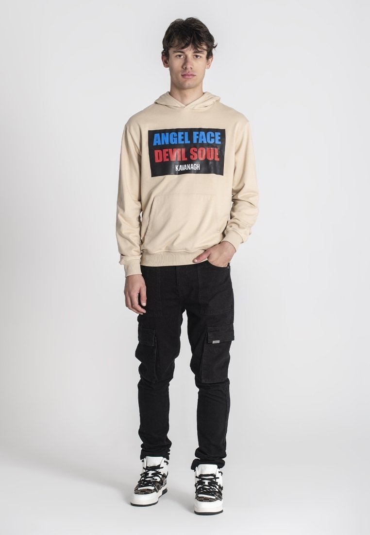 Sudadera beige con la impresión "ANGEL FACE DEVIL SOUL" en azul y rojo. Pantalones cargo negros con bolsillos, combinados con zapatillas en blanco y negro.