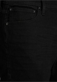 Pantalones vaqueros de mezclilla negra con una textura elegante y suave, detalles de costuras precisas y pequeños adornos metálicos en los bolsillos. Diseño ajustado, estilo clásico de cinco bolsillos.